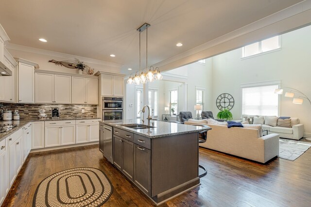 kitchen with sink, light stone counters, a kitchen island with sink, decorative backsplash, and white cabinets