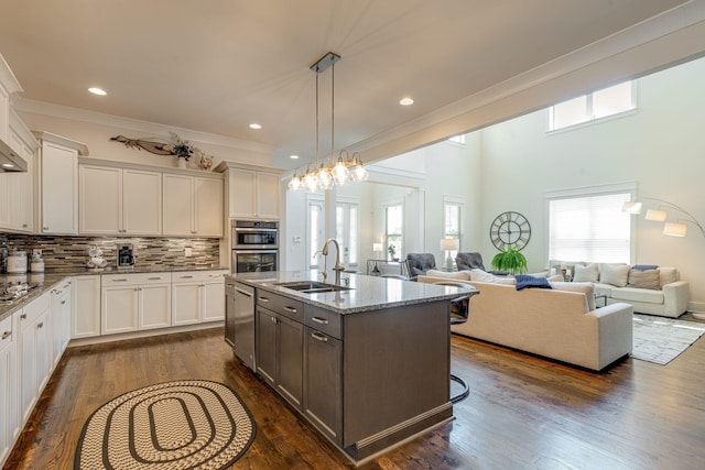 kitchen with sink, light stone counters, a kitchen island with sink, decorative backsplash, and white cabinets