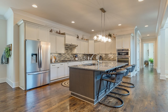 kitchen with a breakfast bar, sink, appliances with stainless steel finishes, dark stone counters, and a kitchen island with sink