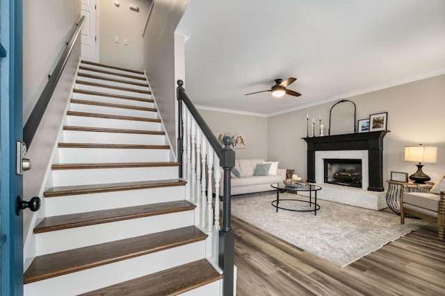 living room featuring ceiling fan, ornamental molding, a brick fireplace, and light hardwood / wood-style flooring