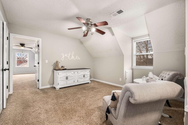 living area with ceiling fan, light colored carpet, lofted ceiling, and a textured ceiling