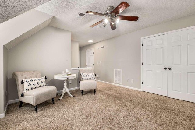 living area featuring vaulted ceiling, ceiling fan, carpet, and a textured ceiling