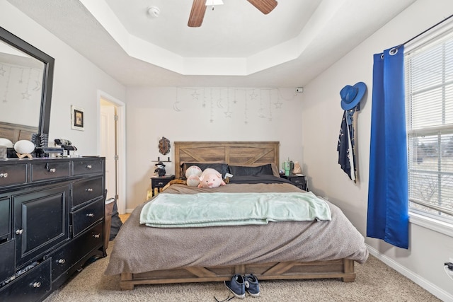 carpeted bedroom with a raised ceiling and ceiling fan