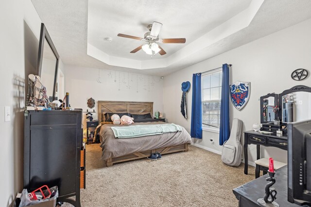 carpeted bedroom with a raised ceiling and ceiling fan