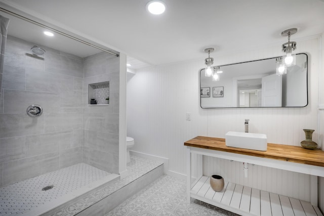 bathroom with tile patterned flooring, vanity, a tile shower, and toilet