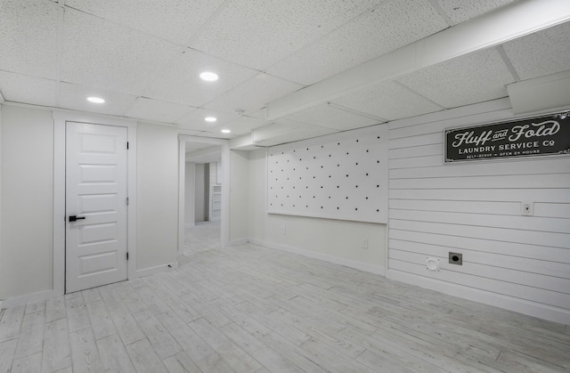 basement with a paneled ceiling, wooden walls, light hardwood / wood-style flooring, and a mail area