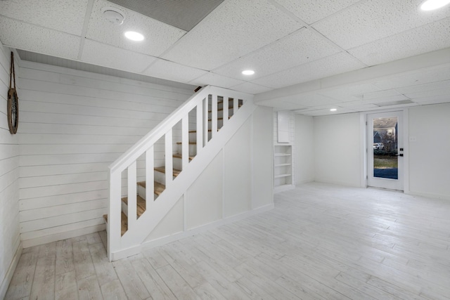 basement featuring wooden walls, a paneled ceiling, and light hardwood / wood-style floors