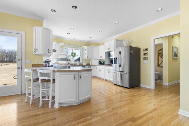 kitchen with stainless steel appliances, ornamental molding, white cabinets, and decorative light fixtures