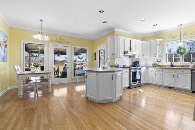 kitchen with appliances with stainless steel finishes, white cabinets, decorative light fixtures, kitchen peninsula, and light wood-type flooring