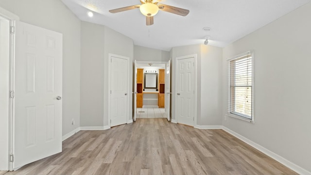 unfurnished bedroom featuring connected bathroom, two closets, light hardwood / wood-style floors, and ceiling fan