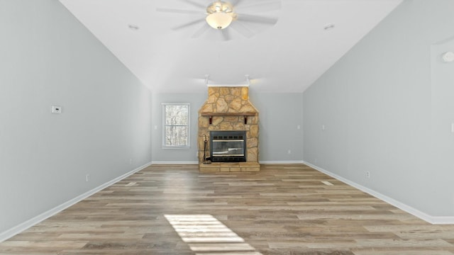 unfurnished living room with vaulted ceiling, a stone fireplace, ceiling fan, and light hardwood / wood-style flooring