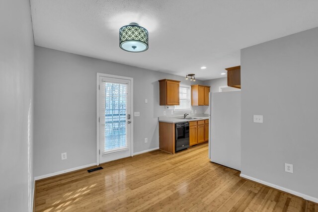 kitchen with white refrigerator, black dishwasher, sink, and light wood-type flooring