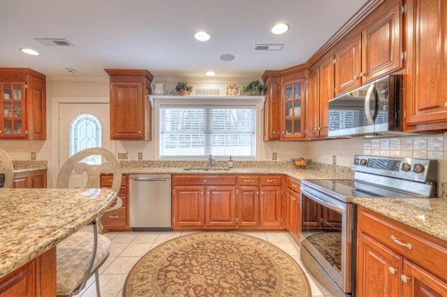 kitchen with a healthy amount of sunlight, appliances with stainless steel finishes, light stone countertops, and sink