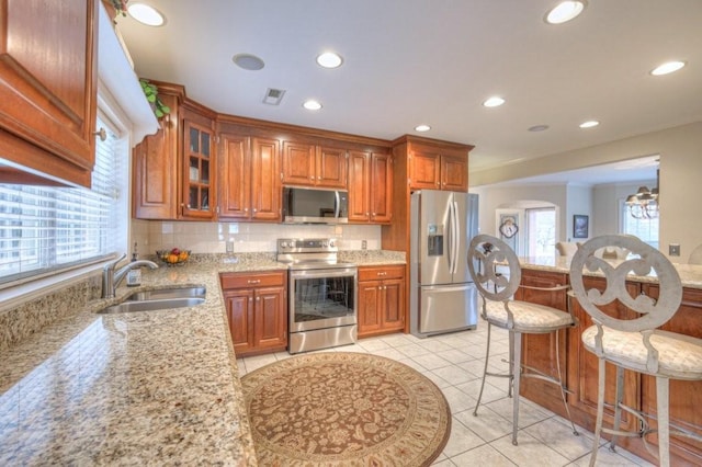 kitchen with a kitchen bar, sink, light stone counters, light tile patterned floors, and stainless steel appliances