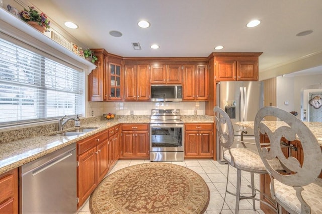 kitchen with sink, light tile patterned floors, appliances with stainless steel finishes, backsplash, and light stone countertops