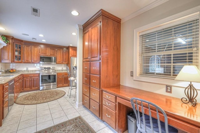 kitchen featuring light tile patterned flooring, sink, crown molding, built in desk, and stainless steel appliances