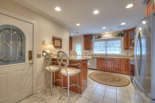 kitchen with a kitchen bar, sink, ornamental molding, appliances with stainless steel finishes, and light stone countertops