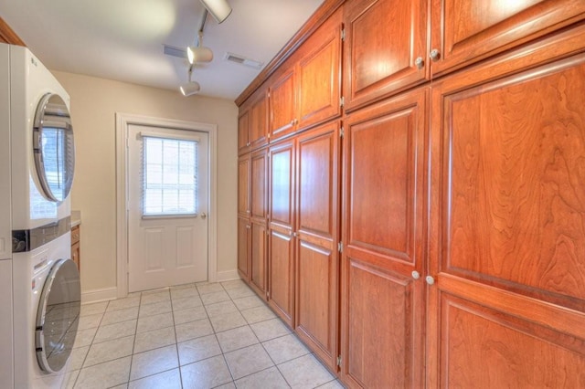 laundry area featuring cabinets, stacked washing maching and dryer, light tile patterned floors, and track lighting