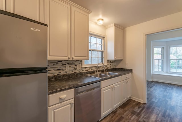 kitchen featuring stainless steel appliances, a sink, backsplash, a wealth of natural light, and dark countertops