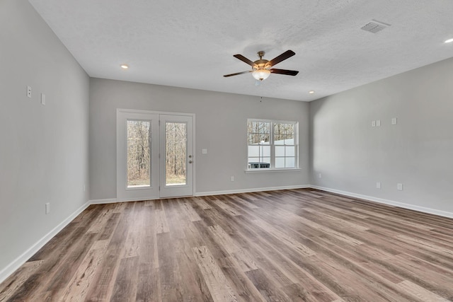 unfurnished living room with a textured ceiling, wood finished floors, visible vents, and baseboards