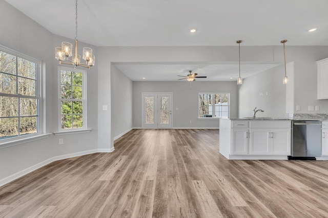 kitchen featuring white cabinets, light stone counters, open floor plan, stainless steel dishwasher, and a sink