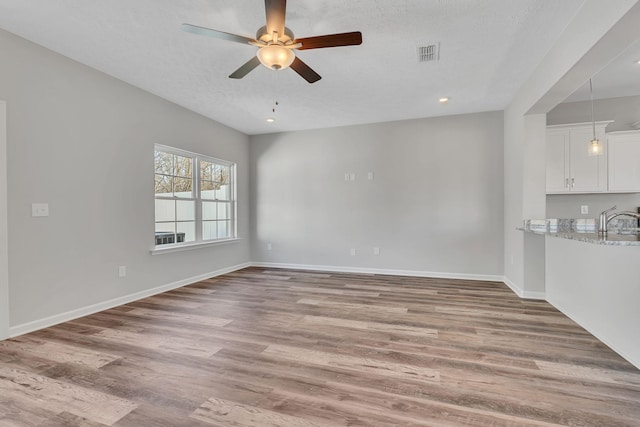 unfurnished living room with baseboards, visible vents, a ceiling fan, wood finished floors, and a sink