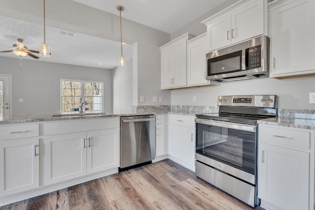 kitchen with white cabinets, stainless steel appliances, a sink, and decorative light fixtures