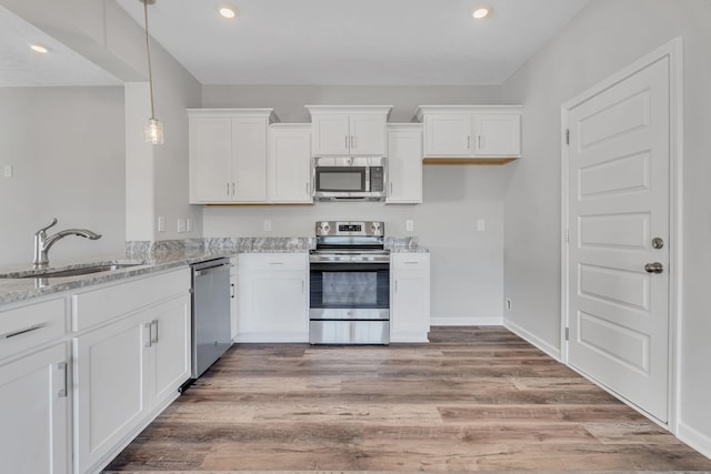 kitchen featuring stainless steel appliances, pendant lighting, white cabinetry, and light stone counters