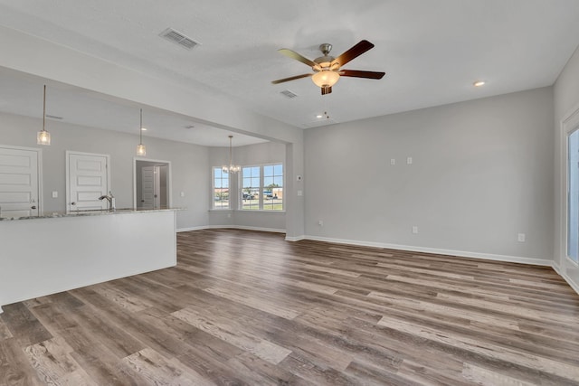 unfurnished living room with baseboards, visible vents, wood finished floors, and ceiling fan with notable chandelier