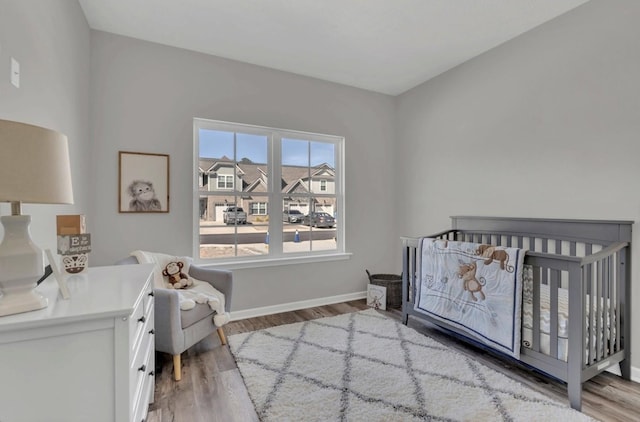 bedroom featuring light wood-style floors, a crib, and baseboards