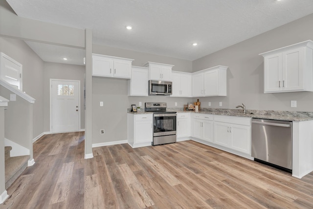 kitchen featuring stainless steel appliances, white cabinetry, light wood-style flooring, and light stone countertops