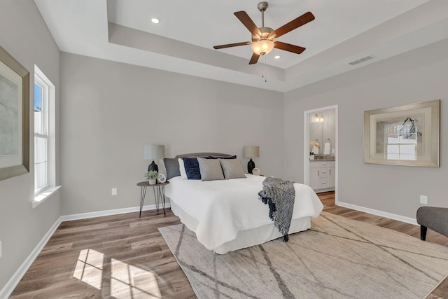 bedroom with a raised ceiling, wood finished floors, visible vents, and baseboards