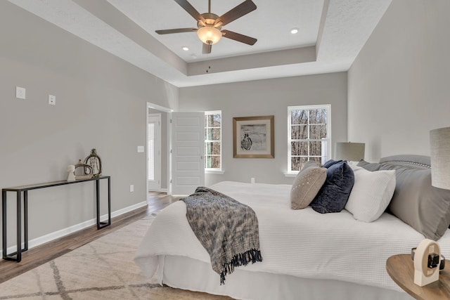 bedroom featuring a tray ceiling, recessed lighting, wood finished floors, and baseboards