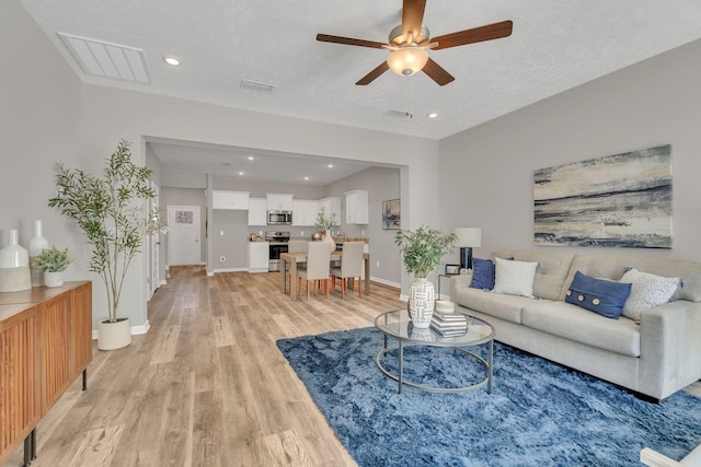 living room with a textured ceiling, light wood finished floors, visible vents, and baseboards