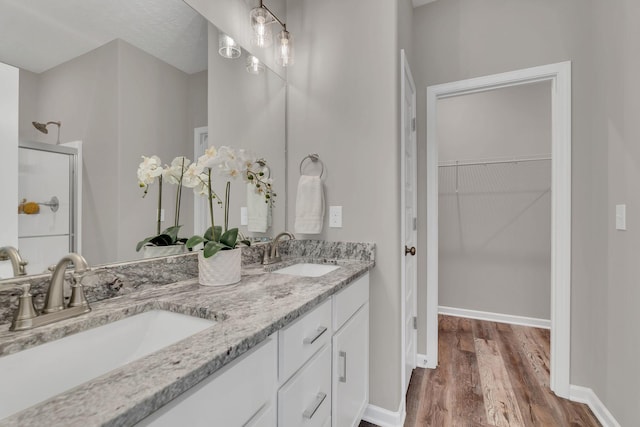 full bathroom with a sink, wood finished floors, a walk in closet, and a shower stall