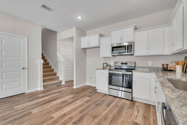 kitchen with visible vents, appliances with stainless steel finishes, light wood-style floors, white cabinets, and light stone countertops