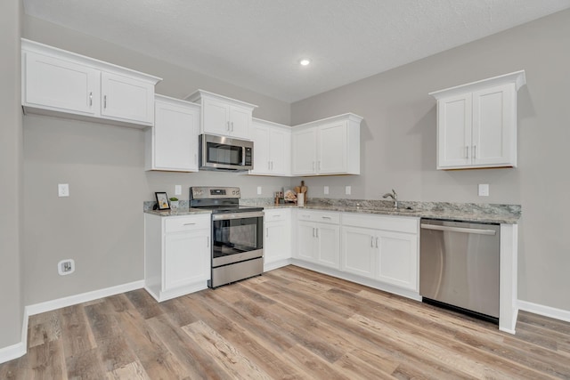 kitchen with light wood finished floors, appliances with stainless steel finishes, white cabinetry, light stone countertops, and baseboards