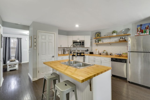 kitchen featuring wooden counters, white cabinetry, a kitchen breakfast bar, stainless steel appliances, and an island with sink