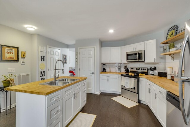 kitchen featuring appliances with stainless steel finishes, white cabinetry, butcher block counters, sink, and a center island with sink