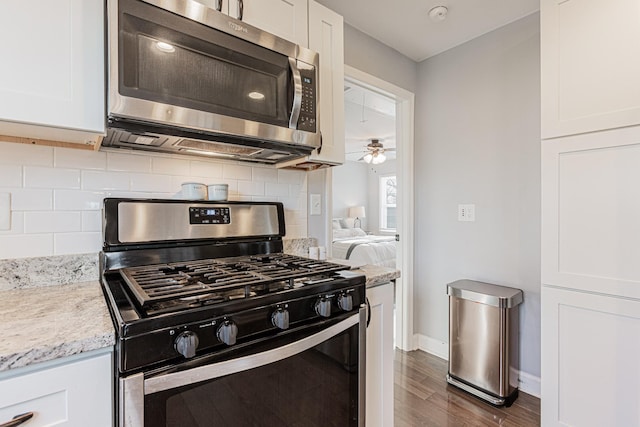 kitchen with appliances with stainless steel finishes, white cabinetry, dark hardwood / wood-style floors, tasteful backsplash, and light stone countertops