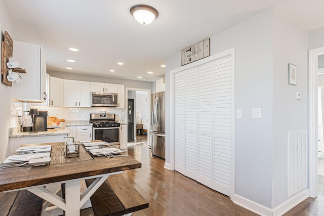 kitchen with backsplash, dark hardwood / wood-style floors, white cabinets, and appliances with stainless steel finishes