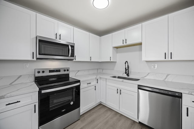 kitchen with stainless steel appliances, sink, white cabinets, and light hardwood / wood-style flooring