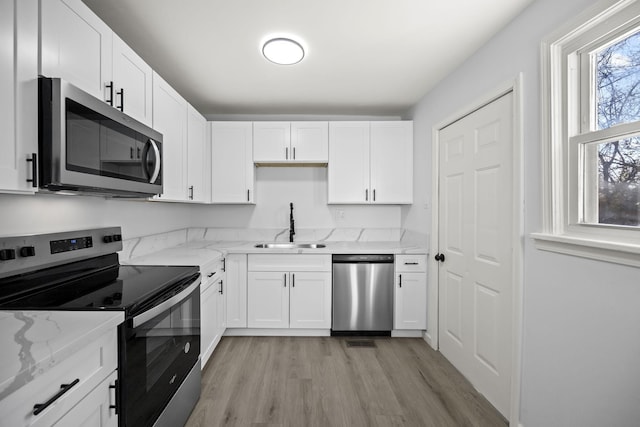 kitchen with sink, light stone counters, white cabinetry, light hardwood / wood-style flooring, and appliances with stainless steel finishes