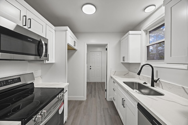 kitchen with appliances with stainless steel finishes, sink, white cabinets, and light hardwood / wood-style floors