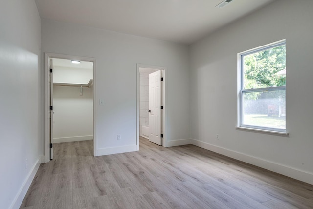 unfurnished bedroom with connected bathroom, a walk in closet, a closet, and light wood-type flooring