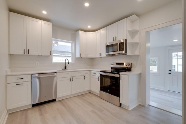 kitchen with stainless steel appliances, white cabinetry, sink, and light hardwood / wood-style floors