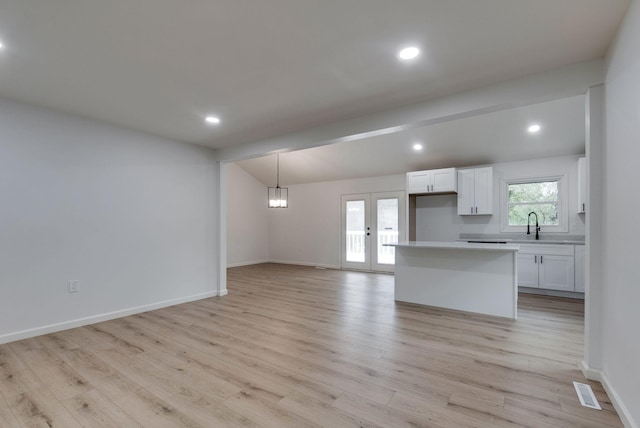 interior space featuring lofted ceiling, white cabinetry, decorative light fixtures, french doors, and light wood-type flooring