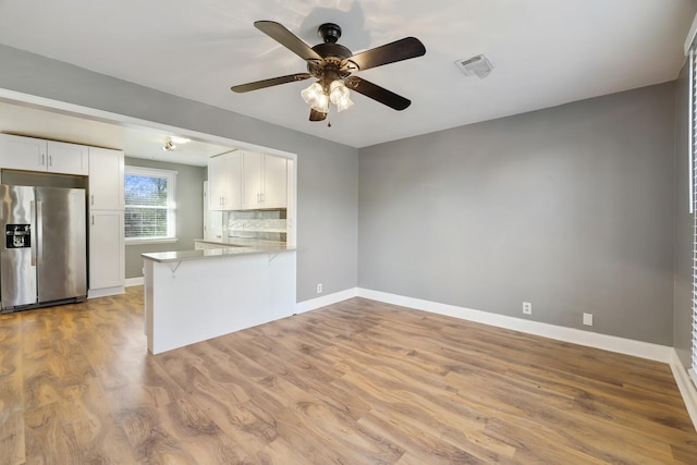 kitchen featuring stainless steel fridge with ice dispenser, backsplash, white cabinets, kitchen peninsula, and light wood-type flooring