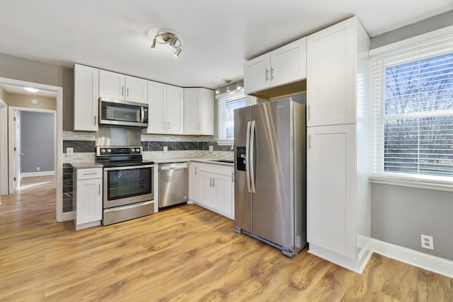 kitchen with decorative backsplash, light hardwood / wood-style flooring, white cabinets, and appliances with stainless steel finishes