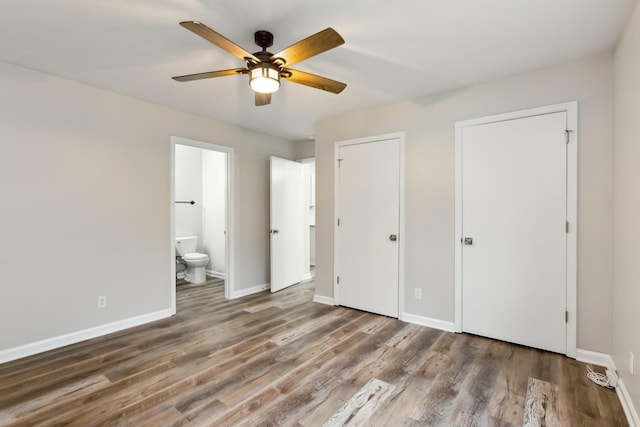 unfurnished bedroom featuring ceiling fan, dark hardwood / wood-style floors, two closets, and ensuite bath